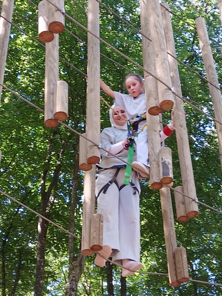 Une adulte accompagne une enfant sur un parcours suspendu
